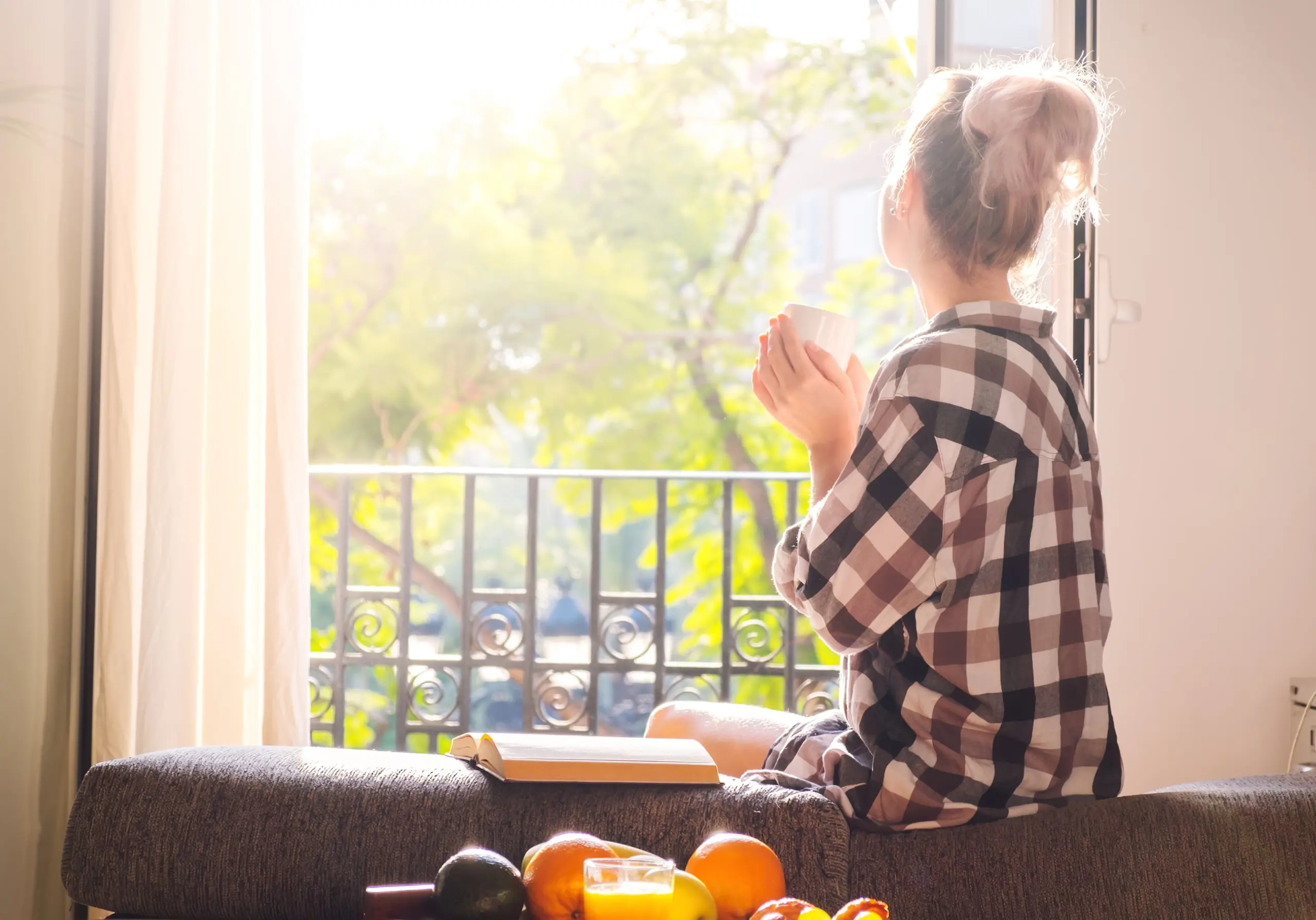 Person looking out a window contemplatively with sunlight streaming in