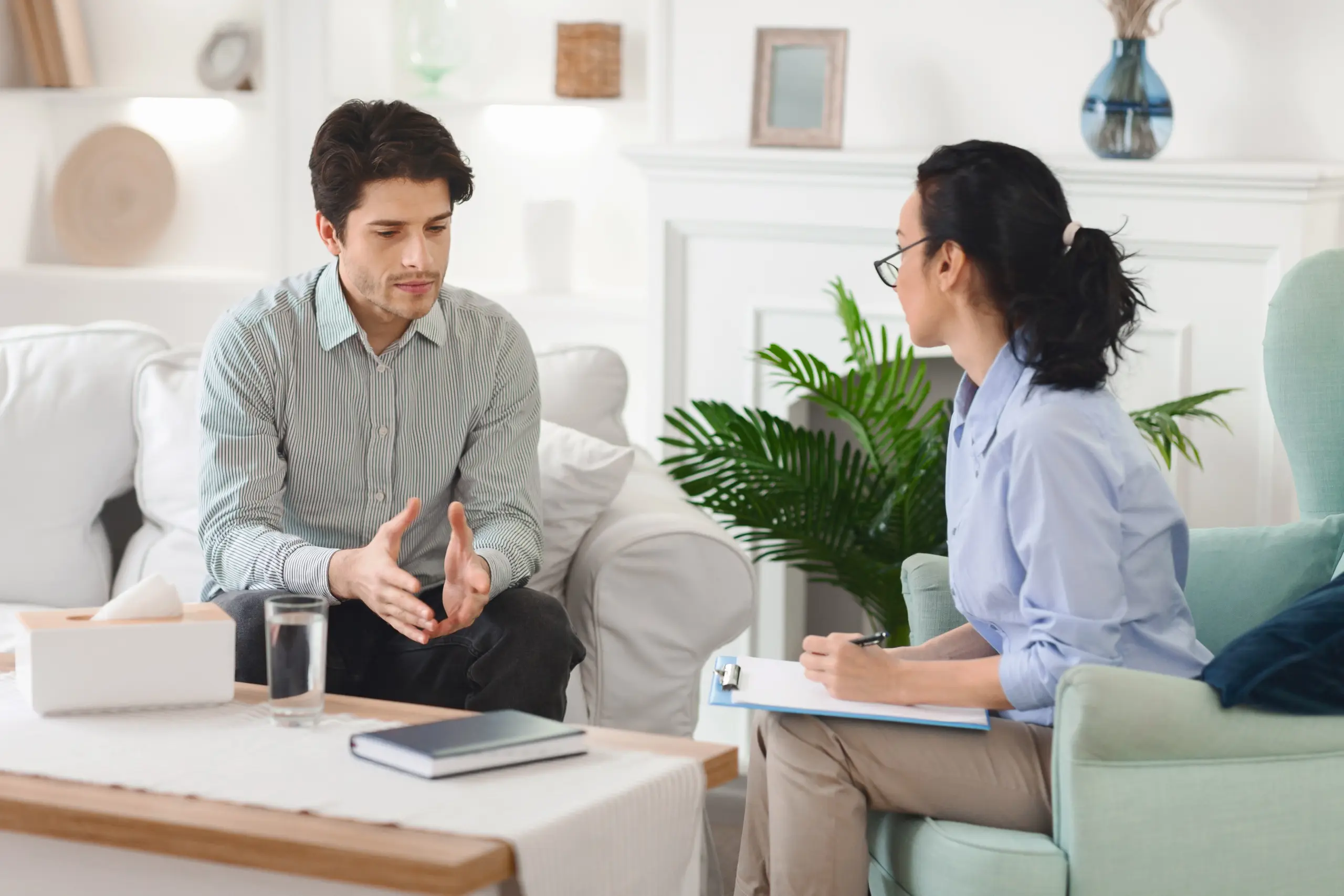 A supportive counselor speaking with a client in a calm therapy room Recovery center professional providing support to client